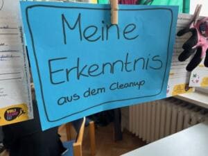 Eine blaue Karte mit der handgeschriebenen Überschrift Meine Erkenntnis aus dem Cleanup hängt mit einer Wäscheklammer an einer Leine.