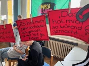 An einer Leine im Klassenzimmer hängen rote Karten mit handgeschriebenen Sätzen wie Es hat mich sehr nachdenklich gemacht, so viel Müll zu finden; dahinter Schülerinnen und eine World-Cleanup-Day-Fahne.