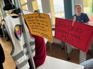 An einer Leine hängen eine Warnweste und zwei Karten mit den Sätzen Es gab sooo viel Müll und Wenn an einem kleinen Ort schon so viel Müll liegt, wie viel liegt dann in der gesamten Umwelt? von der Klasse 6a.