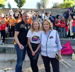 Ein Mann und zwei Frauen, darunter Bundesumweltministerin Steffi Lemke, posieren vor den Stufen des Mauerpark-Amphitheaters voller Teilnehmender; eine trägt ein World-Cleanup-Day-T-Shirt, eine eine Weste und Greifzange.