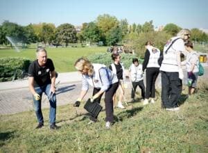 Mehrere Erwachsene in World-Cleanup-Day-Westen, darunter Bundesumweltministerin Steffi Lemke, sammeln mit Greifzangen und Eimern Müll auf einem Grashang im Mauerpark.