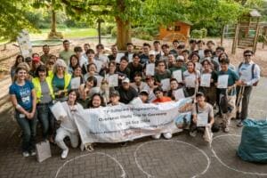 Eine große Gruppe junger Studierender mit Urkunden posiert hinter einem Banner einer Studienreise nach Deutschland, dazu Helferinnen in Warnwesten.