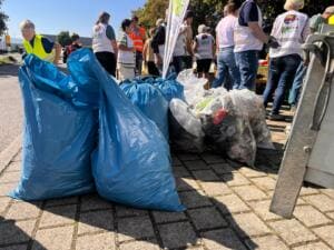 Viele gefüllte blaue und durchsichtige Müllsäcke stehen auf einem gepflasterten Platz, dahinter Helfende in Warnwesten.