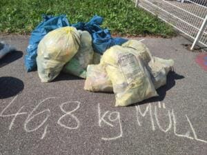 Gefüllte gelbe und blaue Müllsäcke stehen auf dem Asphalt, davor steht mit Kreide 46,8 kg Müll geschrieben.