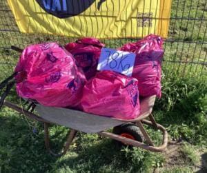 Eine Schubkarre voller pinker World-Cleanup-Day-Säcke mit einem Schild 78 Kg steht vor einer gelben World-Cleanup-Day-Fahne.