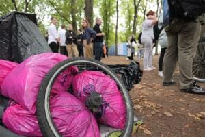 Im Vordergrund liegen gefüllte pinke World-Cleanup-Day-Säcke und ein altes Fahrradrad, dahinter stehen Helfende im Park.