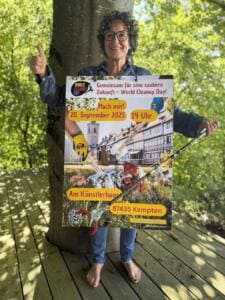 Eine Frau hält unter einem Baum ein Plakat zum World Cleanup Day am 20. September 2025 in Kempten sowie eine Greifzange und zeigt den Daumen hoch.