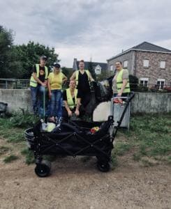 Fünf Erwachsene in gelben Warnwesten stehen an einer Mauer neben einem vollen Bollerwagen und einem Einkaufswagen.