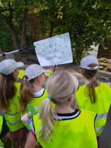 Kita-Kinder in gelben Warnwesten stehen von hinten fotografiert vor einem selbstgemalten Schild mit der Aufschrift Wir halten die Natur sauber.